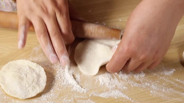 Close up of hands using a wooden rolling pin to roll dough on a floured cutting board to make dumpling wrappers