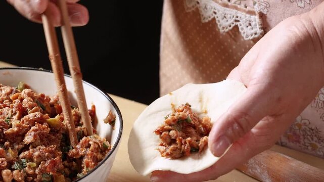 Close-up of hands wrapping handmade Chinese steamed buns with savory pork meat filling on a wooden table