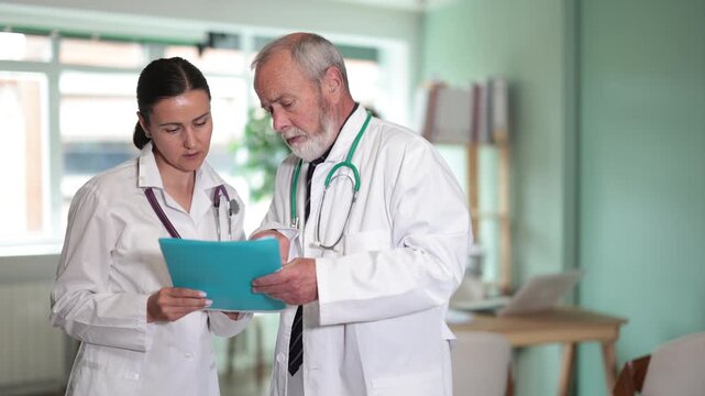  Elderly male and adult female physicians holding paper folder with test results and discussing patient cases