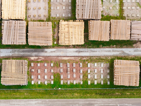 Aerial view of stacked lumber and timber logs arranged in a forestry yard with concrete foundations and surrounding green grass, Latvia.