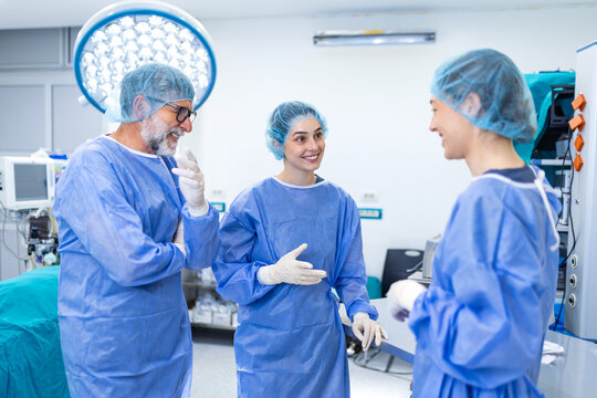 Professional medical team including a surgeon and assistants discussing after a successful operation in an operating room. Happy doctors in blue scrubs communicate about the patient procedure.
