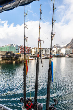 Fishing rods are ready for use in the harbor of Svolvaer, Lofoten, Norway on a bright day with cabins and mountains in the background