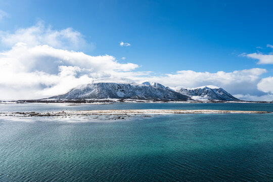 Landscape in the Vesteralen islands in Norway with snow covered mountains and blue sky, seen from the water