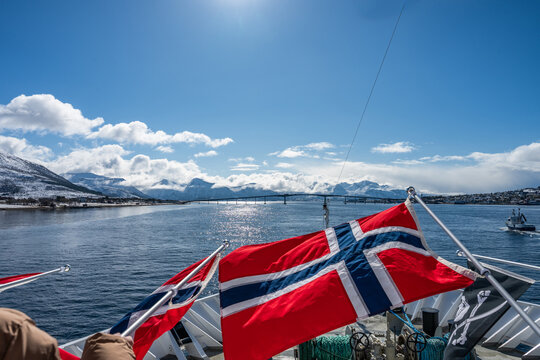 Norwegian flags are being waved on a ship approaching the bridge of the small town of Sortland. Vesteralen, Norway.