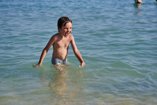 A cheerful child enjoys wading and splashing in the calm turquoise ocean waves at a sunny beach resort.