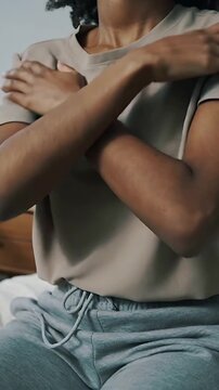 Vertical video: Opening eyes, woman in beige tee gray sweats adjusting self-hug on bed, drawstring