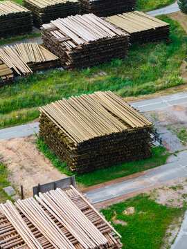 Aerial view of stacked timber logs in a lumber yard surrounded by green grass and paved paths in Brankas, Jelgava Municipality, Latvia.