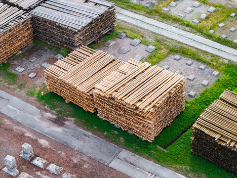 Aerial view of large stacks of timber logs stored in an industrial lumber yard with concrete foundations and patches of green grass in Brankas, Jelgava Municipality, Latvia.