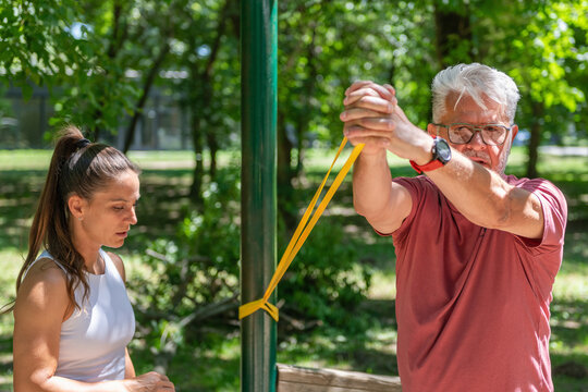 Senior man performing a resistance band shoulder mobility exercise with professional supervision to increase flexibility, joint mobility, upper body control, and overall functional fitness.