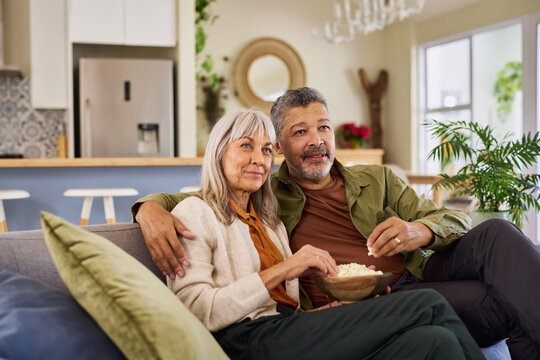 Elder couple watching TV at home while eating popcorn