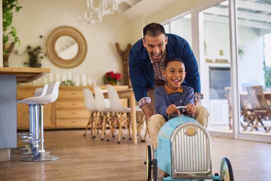 Joyful father pushing  toy car with son at home