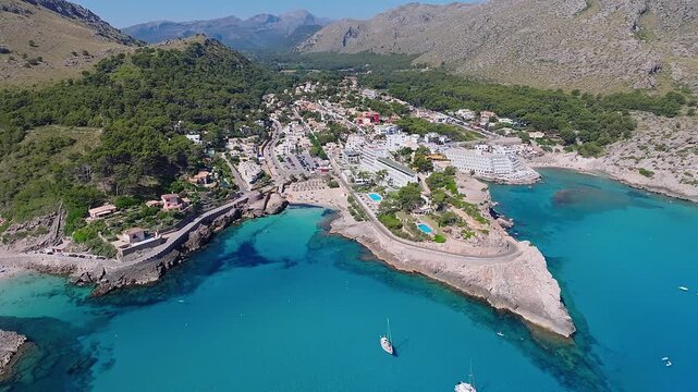Mallorca, Spain - 4K Flying by Cala Sant Vicenc on the island of Mallorca at daytime with Cala Clara and Cala Molins bays, beach, hotels, yachts and mountains at background