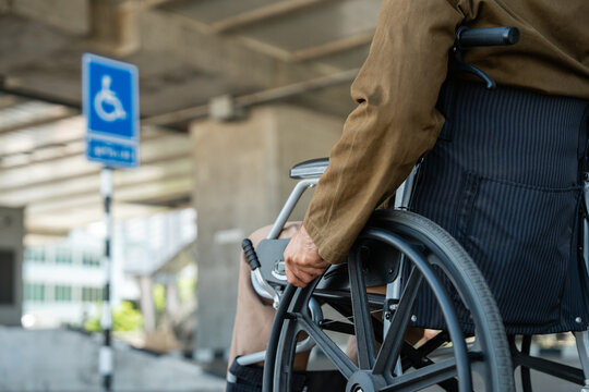 A man with a leg disability who cannot walk uses a wheelchair and travels by the train at a station He walks along the sidewalk where there are signs indicating accessibility for disabled individuals