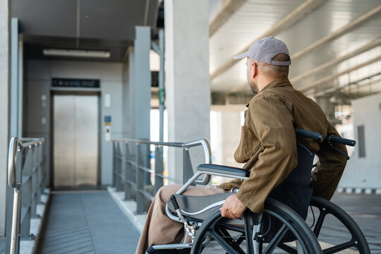 A man with a leg disability who cannot walk uses a wheelchair and travels by the train at a station He walks along the sidewalk where there are signs indicating accessibility for disabled individuals