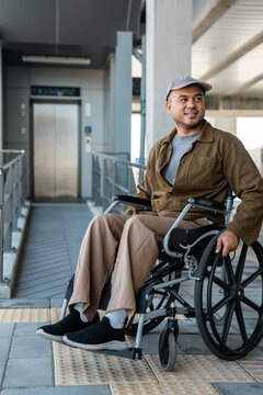 A man with a leg disability who cannot walk uses a wheelchair and travels by the train at a station He walks along the sidewalk where there are signs indicating accessibility for disabled individuals