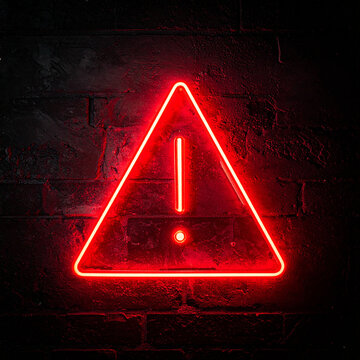 Glowing neon red triangle sign with exclamation point on dark. Warning indicator. Alert signal. Close-up.