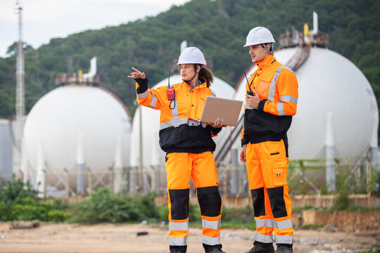 Team of Industrial engineers using laptop and radio to monitor gas storage tank system, Technical team in safety uniform discussing maintenance plan at fuel storage facility