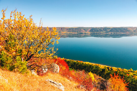 Vibrant autumn panorama overlooking a tranquil lake with turquoise water, embraced by colorful leaves. Atmospheric place in the Dniester canyon, Ukraine, Bakota Bay.