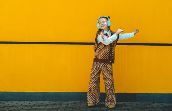 A happy girl enjoys music and dances near a yellow wall