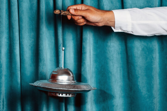 Hand holding a toy UFO prop on a string against a theater curtain
