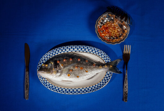 A surreal raw fish with gold jewels rests on a plate