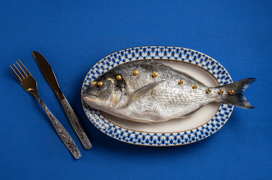 A surreal raw fish with gold beads lies on a plate indoors