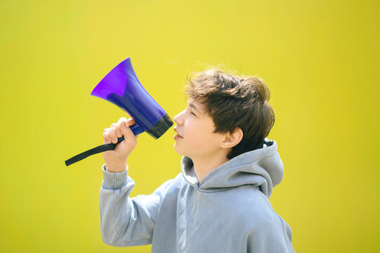 Teenage boy in hoodie shouting through loudspeaker against yellow wall