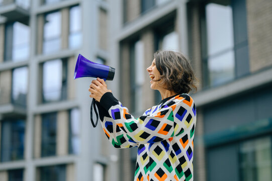 Woman in colorful sweater shouts into loudspeaker during urban rally