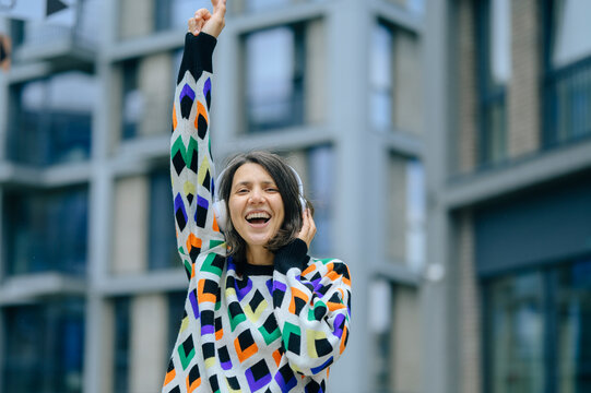 A smiling woman listens to music with headphones in the city