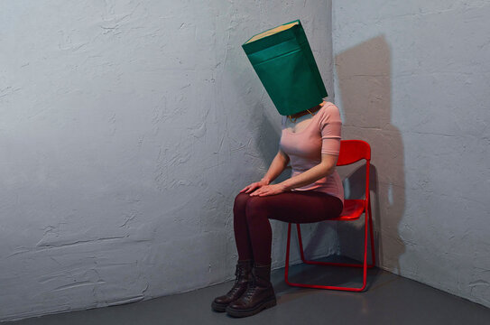 A woman sits on a chair with a paper bag over her head