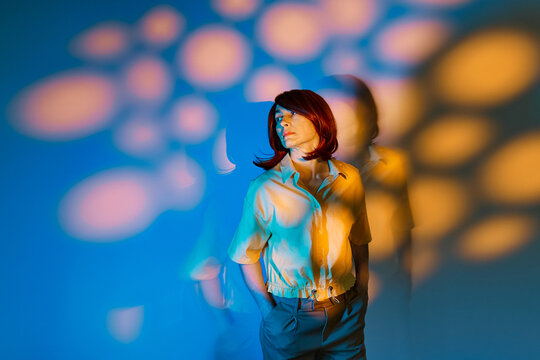 Woman stands indoors with surreal colored lighting and shadow