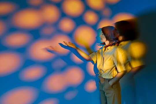 Woman reaches hand toward surreal colored light projection indoors