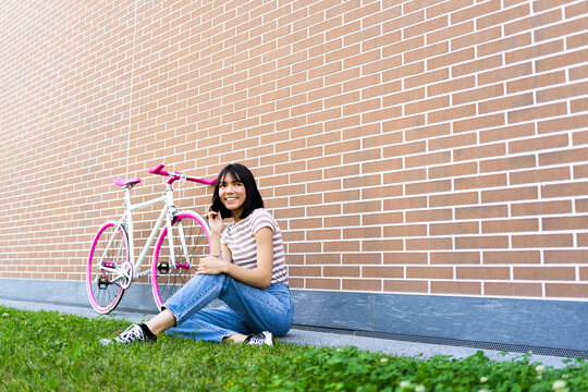 Smiling young woman talking on mobile phone while sitting on footpath