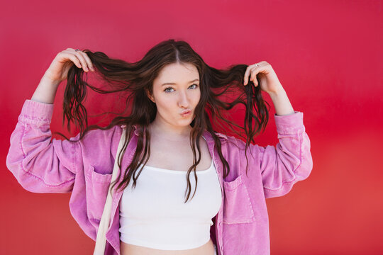 Playful portrait of woman holding long brown hair on red background
