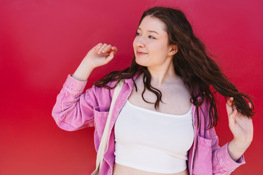 Smiling model playing with hair against vibrant red background
