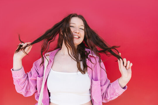 Woman smiling and playing with long brown hair against red background