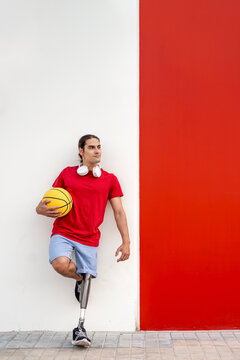 Thoughtful man with disability holding yellow basketball and leaning on wall