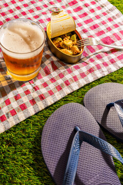 A glass of beer and canned mussels rest on a checkered picnic blanket