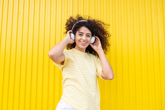 Smiling woman listening to music with headphone on yellow background