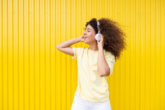 Woman listening to music with headphone on vibrant yellow background