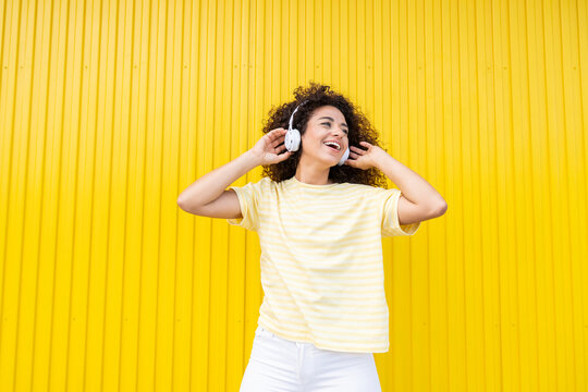 Smiling woman enjoying music with headphone on yellow background