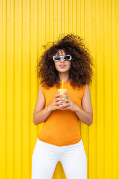 Woman with curly hair holding juice against yellow background