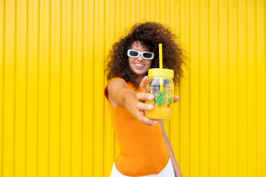 Woman holding jar of juice against yellow background in summer
