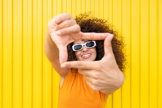 Smiling model with curly hair making hand frame on yellow wall