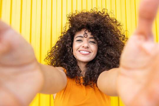 Smiling woman with curly hair reaching out on yellow background