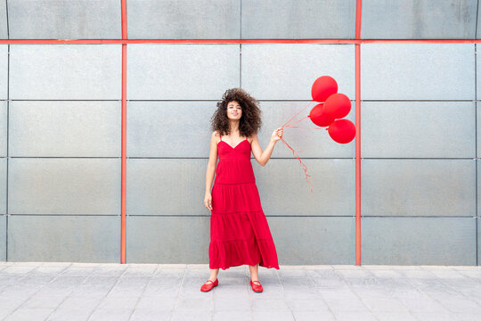 Model in red dress holding red balloons against a grey wall