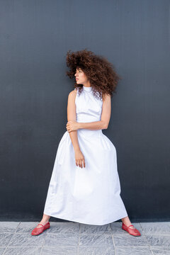 A female model poses in a white dress against a black background