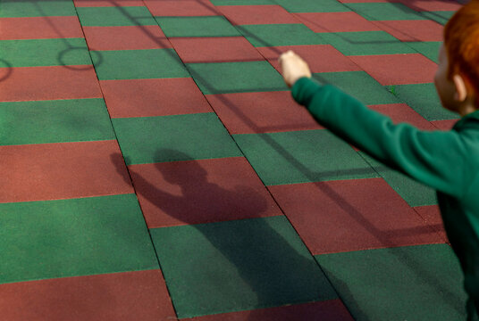 Boy casts a shadow while running on a rubber playground surface