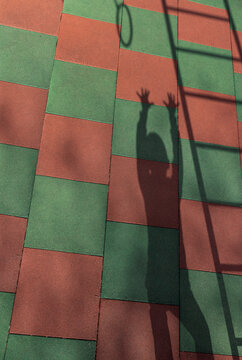 Shadow of a boy reaches for a playground ring on rubber tiles