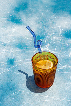 Refreshing lemon drink with blue twisted straw on blue surface